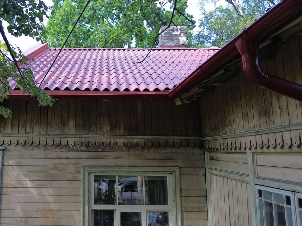 Sarkana tekne un notekcaurule pie koka mājas stūra